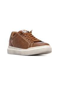 Zapatilla de cuero marrón con un acabado texturizado, con cordones en la parte delantera y una suela de goma blanca. Presenta un branding sutil y una punta redondeada suave.