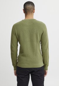 Olivgrüner, gestrickter Pullover mit strukturierter Oberfläche, langen Ärmeln, geripptem Saum und rundem Hals. Hat ein Etikett an der unteren Seite.