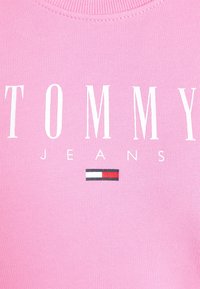 T-shirt en coton rose avec le texte blanc "TOMMY" et "JEANS", avec un petit accent de logo rouge, blanc et bleu en dessous.