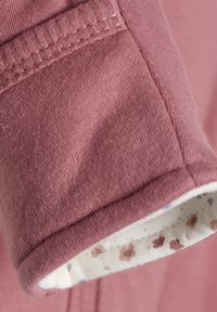 Rosa Baumwollstoff mit geripptem Bündchen, das ein weiches, cremefarbenes Innenfutter mit kleinen braunen und blauen Blumenmustern aufweist.