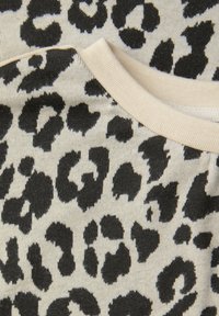 Tkanina w panterkę w kolorach kremowym i czarnym, z nieregularnymi plamkami. Dekolt w kształcie zaokrąglonego kołnierza wykończony jest jednolitym jasnobeżowym obszyciem.