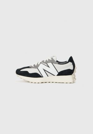 Baskets de sport basses noires, blanches et grises avec grand logo blanc "N" et semelle texturée sur fond clair.
