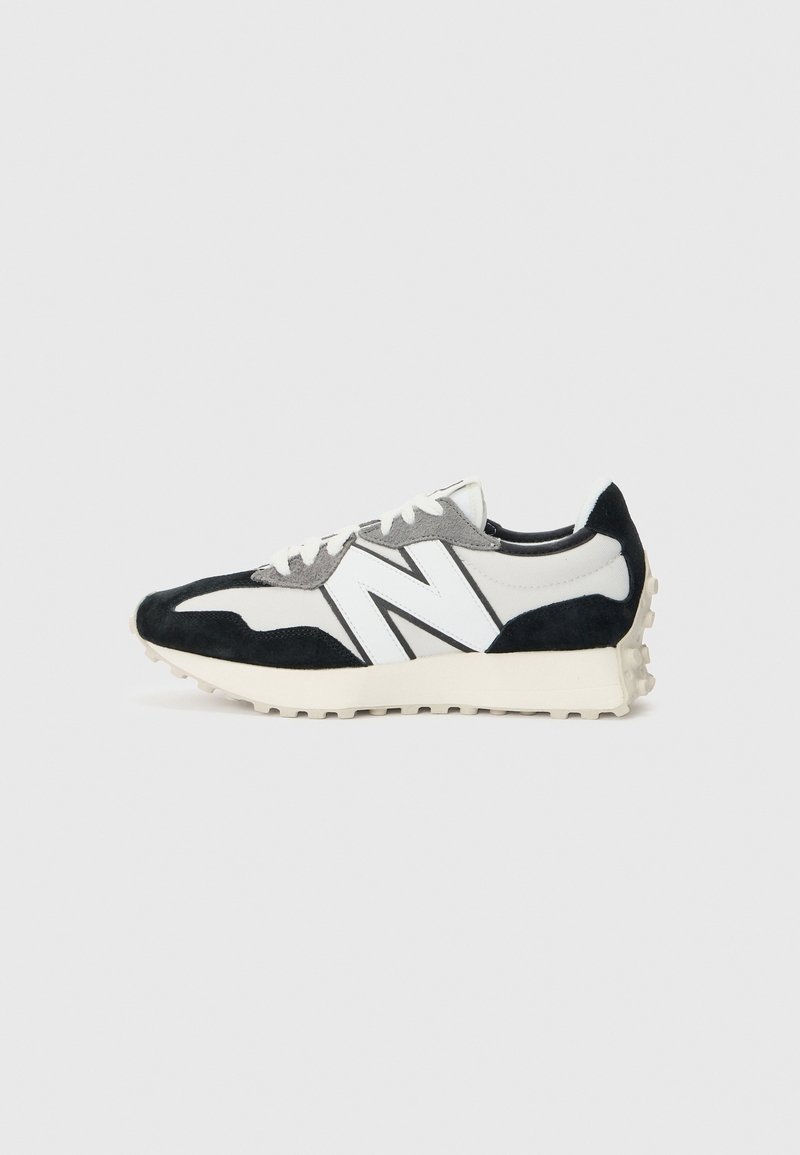 Baskets de sport basses noires, blanches et grises avec grand logo blanc "N" et semelle texturée sur fond clair.