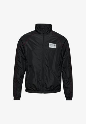 Czarna nylonowa kurtka z wysokim kołnierzem, zamek błyskawiczny z przodu i elastycznymi mankietami. Oferuje kontrastujące czerwone przeszycia oraz naszywkę z logo na piersi.