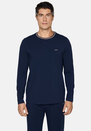 Man met een marineblauw hemd met lange mouwen en bijpassende broek met een klein "JOOP!" logo op de borst en broek.