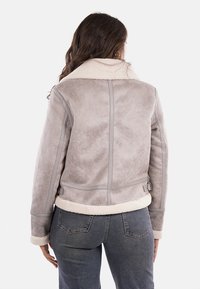 Giacca in pelliccia sintetica grigia con colletto morbido e finitura testurizzata. Presenta un design aderente, cuciture posteriori e fasce laterali regolabili.