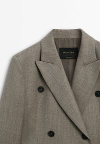 Veste en laine marron croisée à larges revers et boutons noirs, avec une étiquette Massimo Dutti à l'intérieur du col.
