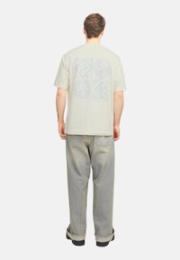 Lys beige oversized T-shirt med et blåt blomstermotiv på ryggen, parret med lyseblå slouchy jeans og sorte sko.