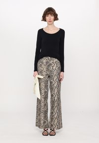 Zwart langemouwen top gecombineerd met wijdvallende faux slangenprint broek in beige en bruin, met een gladde textuur. Houdt een lichte sjaal vast.