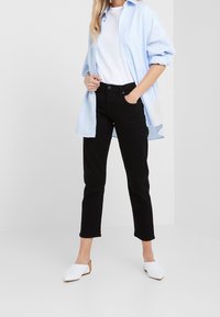 Světle modrá pruhovaná košile na knoflíky, bílý tričko, černé džíny a bílé slip-on boty s hnědými akcenty. Jednoduchý a moderní outfit.