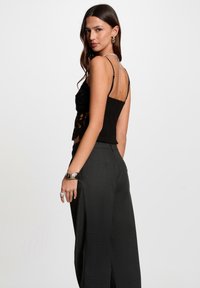 Zwarte kanten top met dunne bandjes, gestructureerde stof en open rugontwerp. Gecombineerd met hooge taille donkere grijze broek. Zilveren sieradenaccenten.