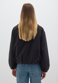 Schwarze, gepolsterte Jacke mit lockerer Passform, mit tailliertem Schnitt und langen Ärmeln. Kombiniert mit hellblauen, hoch taillierten Jeans.
