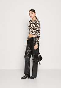 Hosszú ujjú leopárdmintás crop top, magas derekú fekete bőr nadrággal és fekete magassarkú csizmával párosítva, egy kis fekete kézitáskával a kezében.