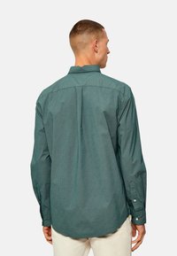 Camisa de manga larga verde con estampado, cuello con botón, y dobladillo redondeado; tejido texturizado con un pequeño diseño geométrico.