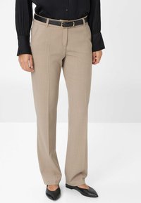 Beige maßgeschneiderte Hosen mit geradem Bein, ausgestattet mit einem schwarzen Gürtel mit goldener Schnalle, kombiniert mit einem langärmeligen schwarzen Oberteil.