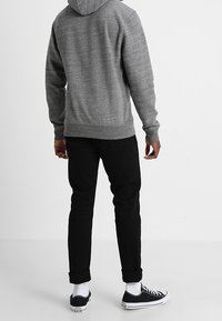 Sudadera gris hecha de un tejido texturizado, con capucha ajustable. Combinada con pantalones negros con puños y zapatillas negras con detalles en blanco.