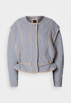 Quilted gray jacket with floral texture, beige piping, round neckline, and subtle waist gathering. Features long sleeves and front closure.