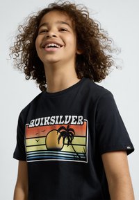 Juodas medvilnės marškinėliai su ryškiu saulėlydžio grafiniu atvaizdu, kuriame matomi geltonos ir oranžinės juostos, palmių medžiai ir tekstas "QUIKSILVER" baltos spalvos.