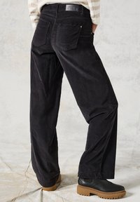 Pantalon en velours côtelé noir à coupe décontractée, avec des poches à l'arrière, associé à des bottes noires en cuir épaisses à semelle épaisse.