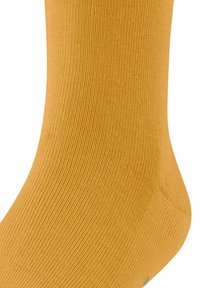 Gros plan sur une chaussette douce et côtelée d'une couleur moutarde vive, mettant en valeur la texture et la forme près de la cheville.