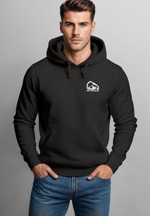Mann mit kurzen braunen Haaren, der einen schwarzen Hoodie mit einem Berg- und Kletterkarabiner-Logo und dem Wort "NEVERLESS" auf der Brust sowie blaue Jeans trägt.