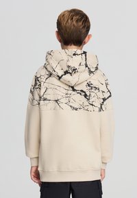 Felpa beige con la parte superiore a motivo marmo nero. Presenta un cappuccio con cordino e polsini a costine, realizzata in un tessuto morbido e testurizzato.