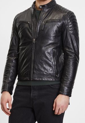Homme portant une veste de motard en cuir noir avec poches poitrine et latérales zippées, détails matelassés aux épaules et col bande avec bouton pression.