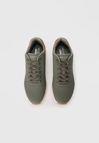 Tenisi sport verzi cu o suprafață netedă, perforată, șireturi și o talpă din cauciuc de o culoare mai deschisă. Prezentă o branță cu marcaj.