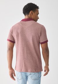 Polo de manga corta en burdeos con un tejido texturizado, cuello y puños de manga en rojo oscuro contrastante, y un dobladillo recto.