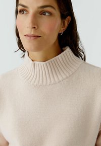 Helles rosa Strickpullover mit hohem, geripptem Kragen und glatter Textur. Der Stoff wirkt weich und gemütlich, ideal für den Casual-Look.