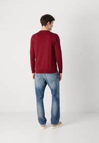 Rød genser med lange ermer og ribbet kant, kombinert med blå denimjeans. Stoffet ser glatt ut og er litt figursydd.