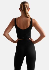 Zwarte geribde crop top met brede schouderbanden, gecombineerd met geribde leggings met hoge taille. Soepele textuur, minimalistisch ontwerp, aansluitende silhouet.
