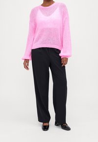 Rosa, genomskinlig stickad tröja med långa ballongsärmar och avslappnad passform, kombinerad med svarta raka byxor och svarta klackar.