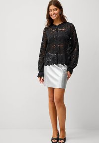 Sort blonde bluse med lange ærmer og rund halsudskæring, parret med en sølv satin mini-nederdel og sorte open-toe hæle.