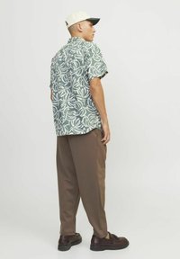 Camicia a maniche corte verde con motivi floreali e foglie bianche; pantaloni marroni dalla vestibilità comoda; persona che indossa un cappellino chiaro e scarpe marroni.