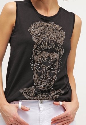 Black sleeveless top with abstract line art of a woman's face and curly hair in a bun, worn with white pants and rings on fingers.