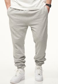 Graue Jogginghosen mit elastischem Bund und Bündchen, die eine lockere Passform bieten. Getragen mit weißen Sneakers, die einen lässigen sportlichen Stil zeigen.