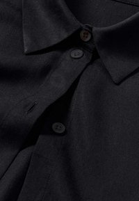 Black button-up shirt with a smooth texture, featuring a classic collar and two front buttons, highlighting a clean and minimalist design.