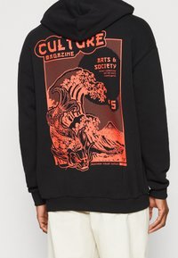 Sudadera negra con una gran gráfica naranja de olas y un dragón, con texto que indica temas culturales y un precio. Tejido suave, capucha ajustable.