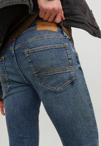 Jeans en denim bleu avec coupe droite, présentant des coutures orange, des poches arrière au design courbe et une étiquette en cuir sur la taille.