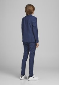 Námorníkově modrý oblek se slim fit kalhotami a upraveným sakem. V kombinaci s bílými teniskami s černými akcenty. Hladká textilie.