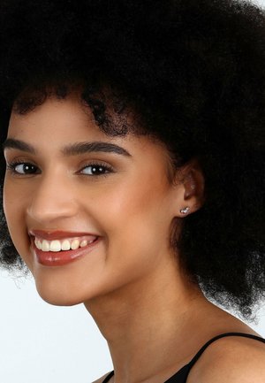 Model mit lockigem schwarzen Haar, trägt diamantförmige Ohrstecker, lächelt und zeigt einen makellosen Teint und natürliches Make-up.