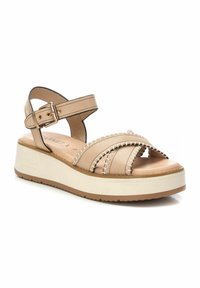 Beige platform sandaaltjes met kruislings leren banden, een gespsluiting rond de enkel en een текстуурste stiksel. Witte zool met lichtbruine profiel.