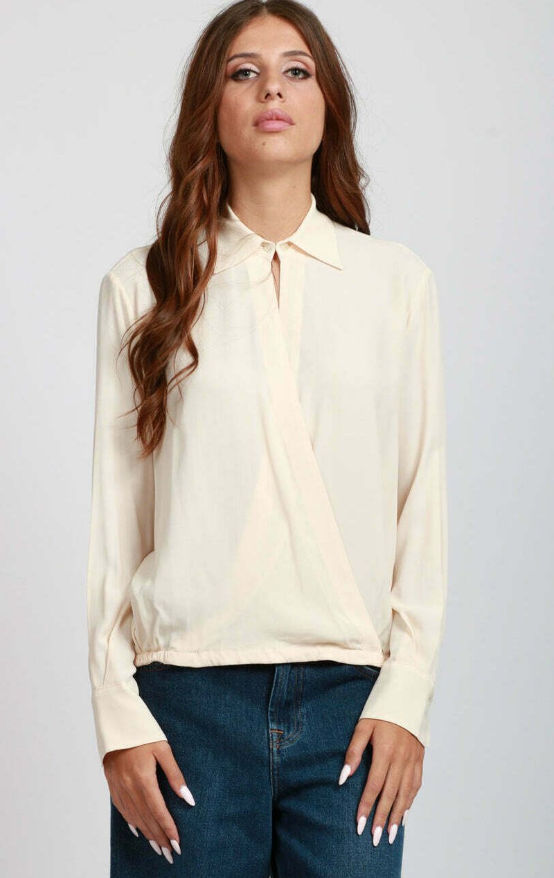 Blusa lunga a maniche con colletto in crema e design avvolgente, caratterizzata da una superficie liscia e da un leggero lucido. Indossata con jeans in denim blu.