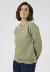 Felpa verde oliva realizzata in misto cotone, con scollatura tonda, polsini a coste e un piccolo logo a forma di cuore rosa sul petto.