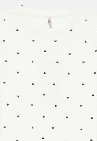 T-shirt branca canelada com um padrão de pequenos corações pretos. Decote redondo, mangas curtas, textura suave e corte descontraído.