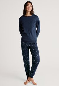 Marineblauw langarmshirt met een borstzak en donkerblauwe pyjamabroek met sterrenpatroon. Zachte stof, aansluitend ontwerp en elastische manchetten.