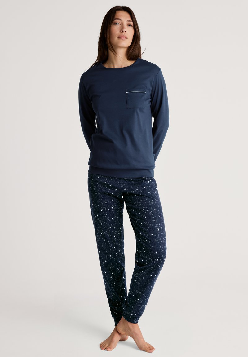 Marineblauw langarmshirt met een borstzak en donkerblauwe pyjamabroek met sterrenpatroon. Zachte stof, aansluitend ontwerp en elastische manchetten.