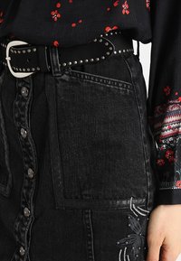 Svart denimkjol med knäppning, sidofickor och broderad blommönster. Matchad med ett svart nubbelt för extra detaljer.