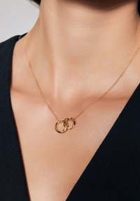 Złoty naszyjnik z dwoma splątanymi, okrągłymi wisiorkami o skręconej fakturze, zawieszonym na delikatnym łańcuszku.